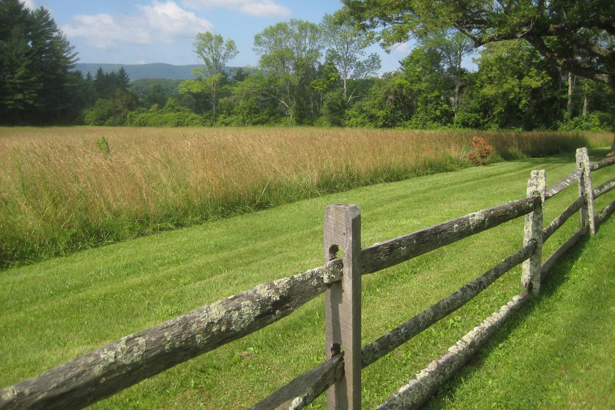 grass fields.one mowed and a wooden fence